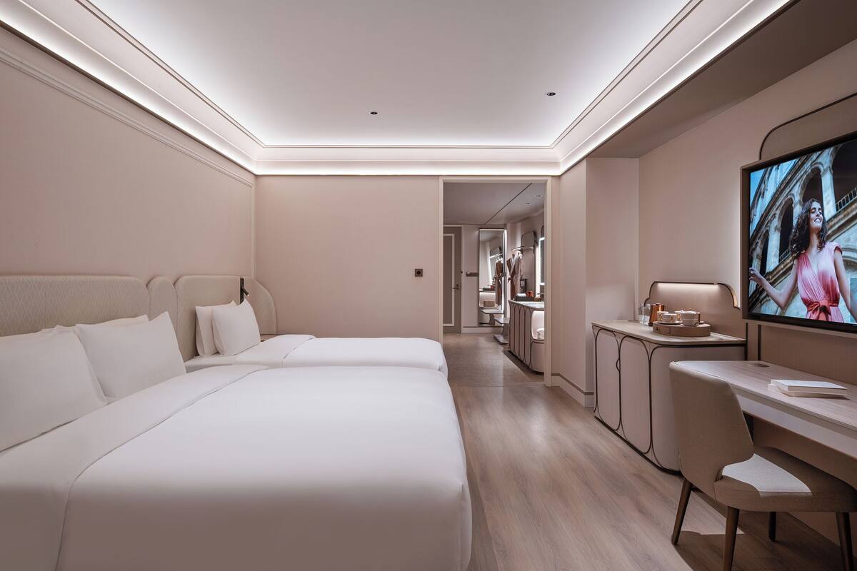 A hotel room with a large bed, a desk, a television, and a view into the hallway.
