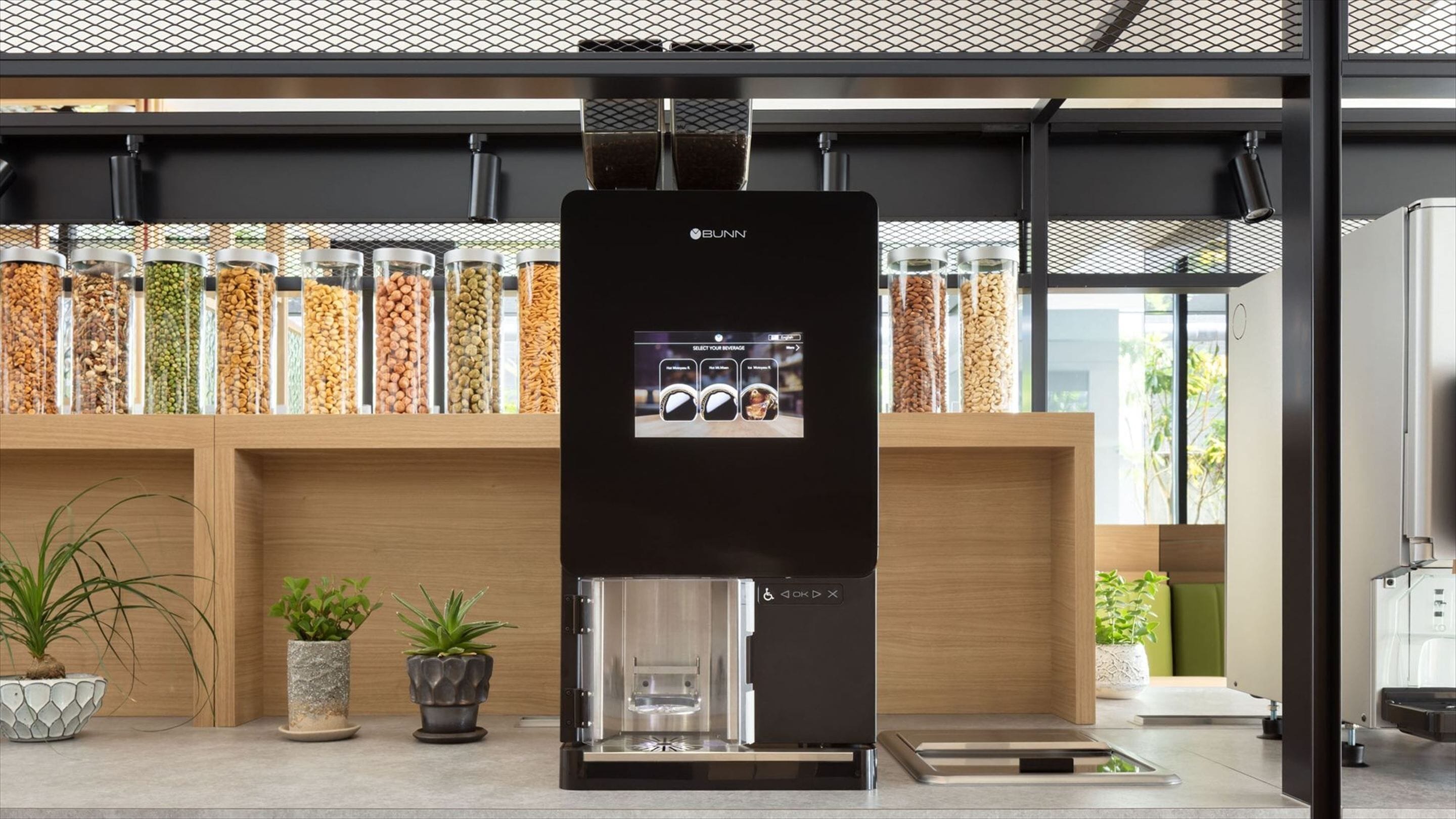 Una cocina moderna con una máquina de café Bunn, diferentes recipientes con cereales y semillas, y plantas en macetas.