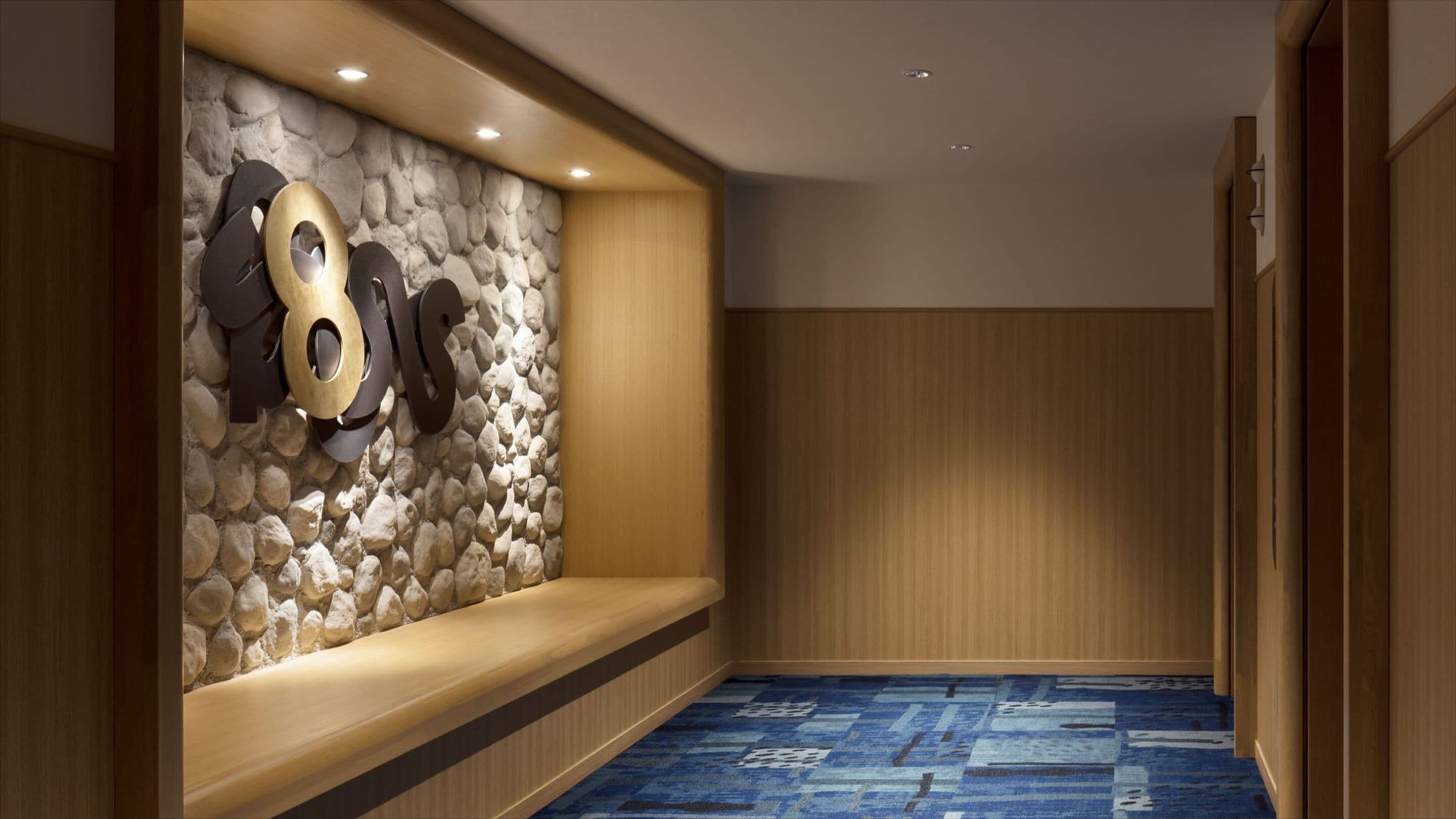 A hallway with a stone wall, a bench, and a patterned carpet.