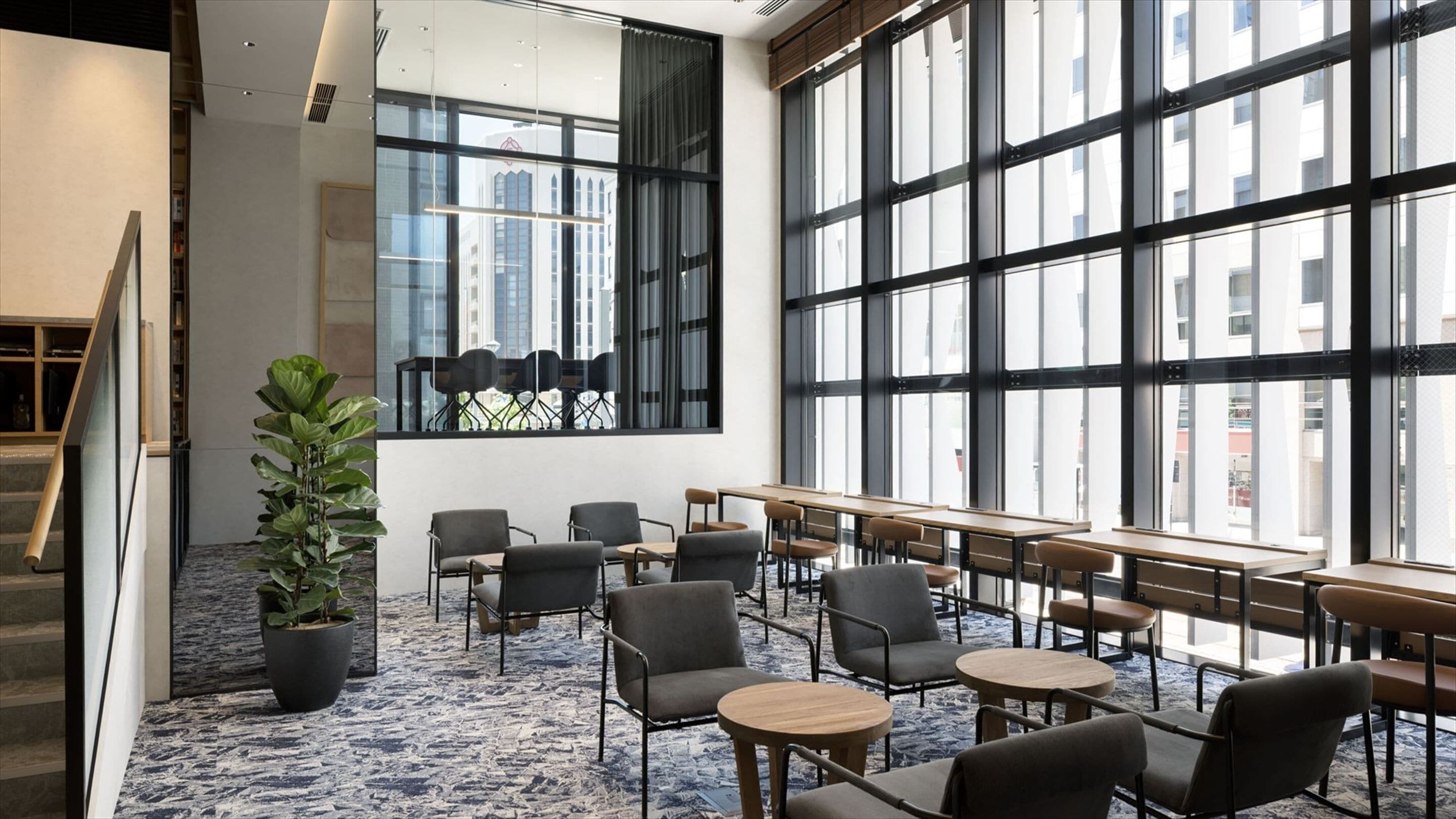 A modern indoor space with large windows, seating arrangements, and a staircase.