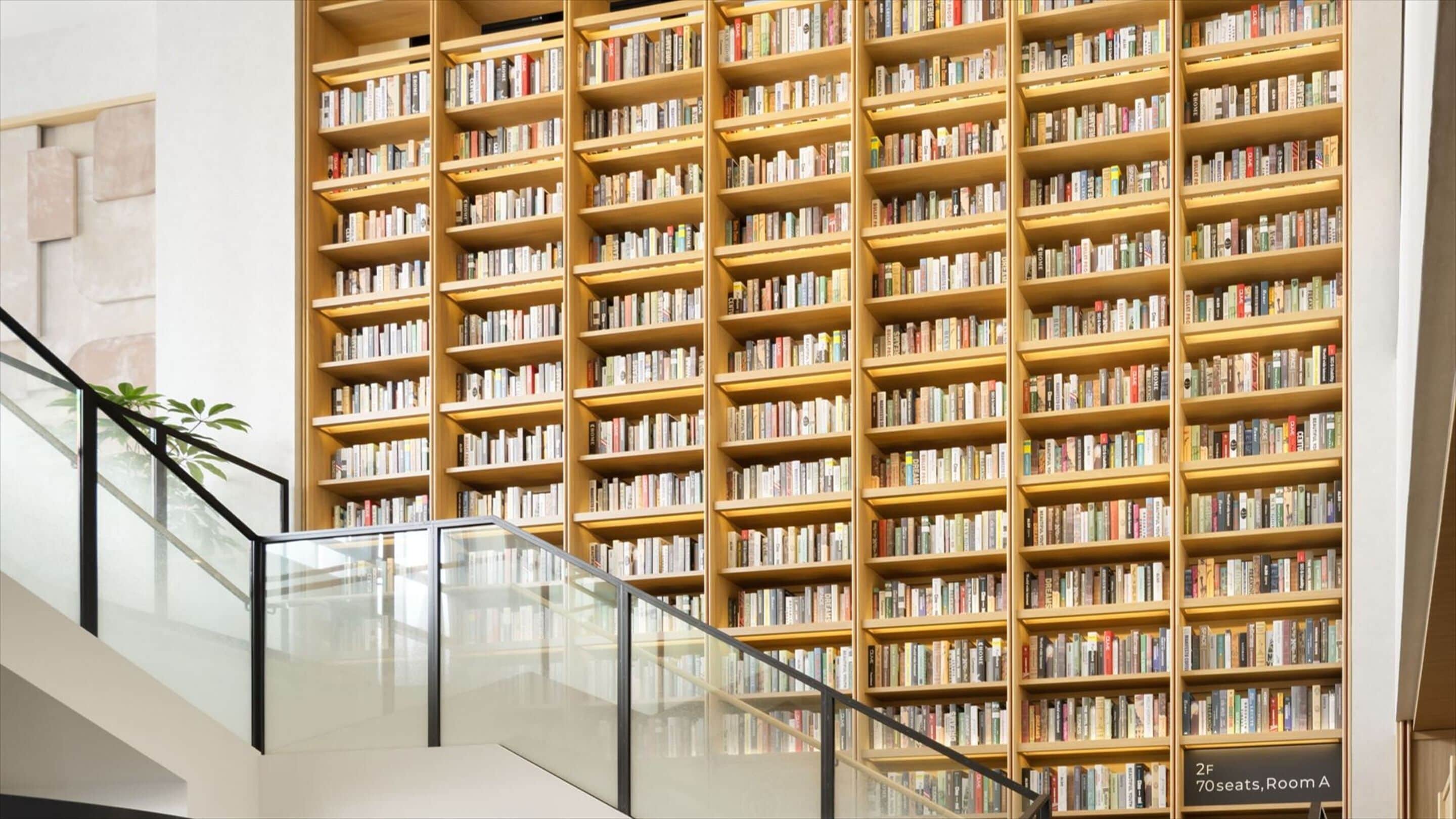 A modern library interior with multiple bookshelves, a glass railing, and a sign indicating '2F 70 seats, Room A'.