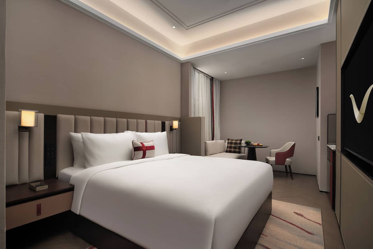 Une chambre d’hôtel moderne, dotée d’un grand lit, de tables de chevet, d’un bureau et d’une chaise.