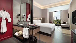 Una habitación de hotel moderna con una cama grande, un baño independiente con tocador, una puerta roja y vistas a la ciudad.