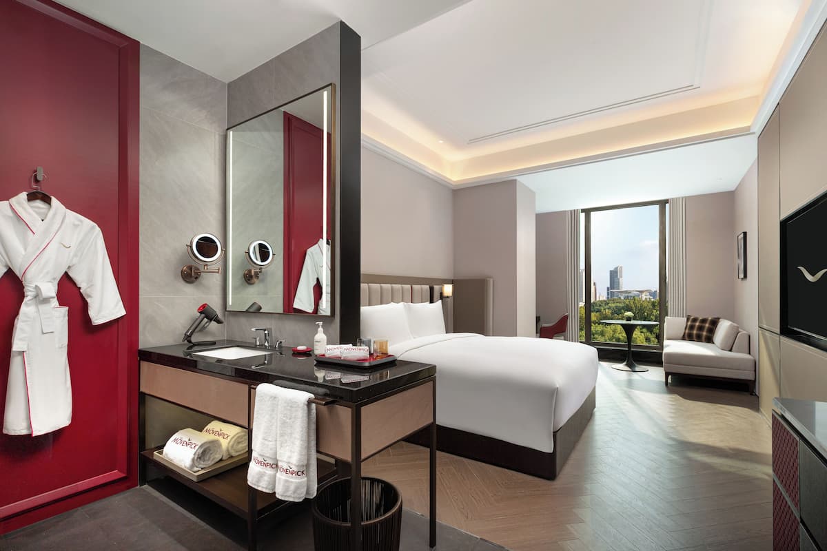 Une chambre d’hôtel moderne avec un grand lit, une salle de bain séparée avec un lavabo, une porte rouge et une vue sur la ville.