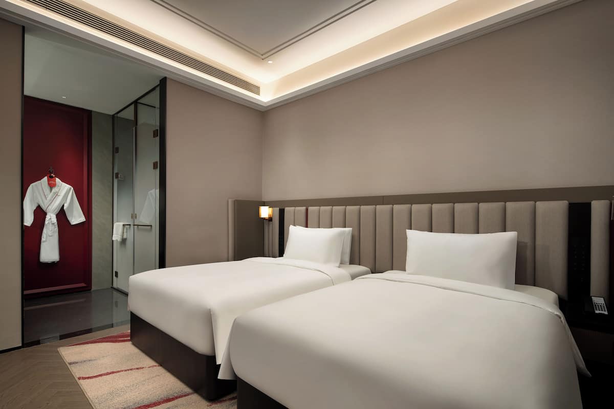 Une chambre d’hôtel avec deux lits, une porte rouge et un peignoir accroché au mur.
