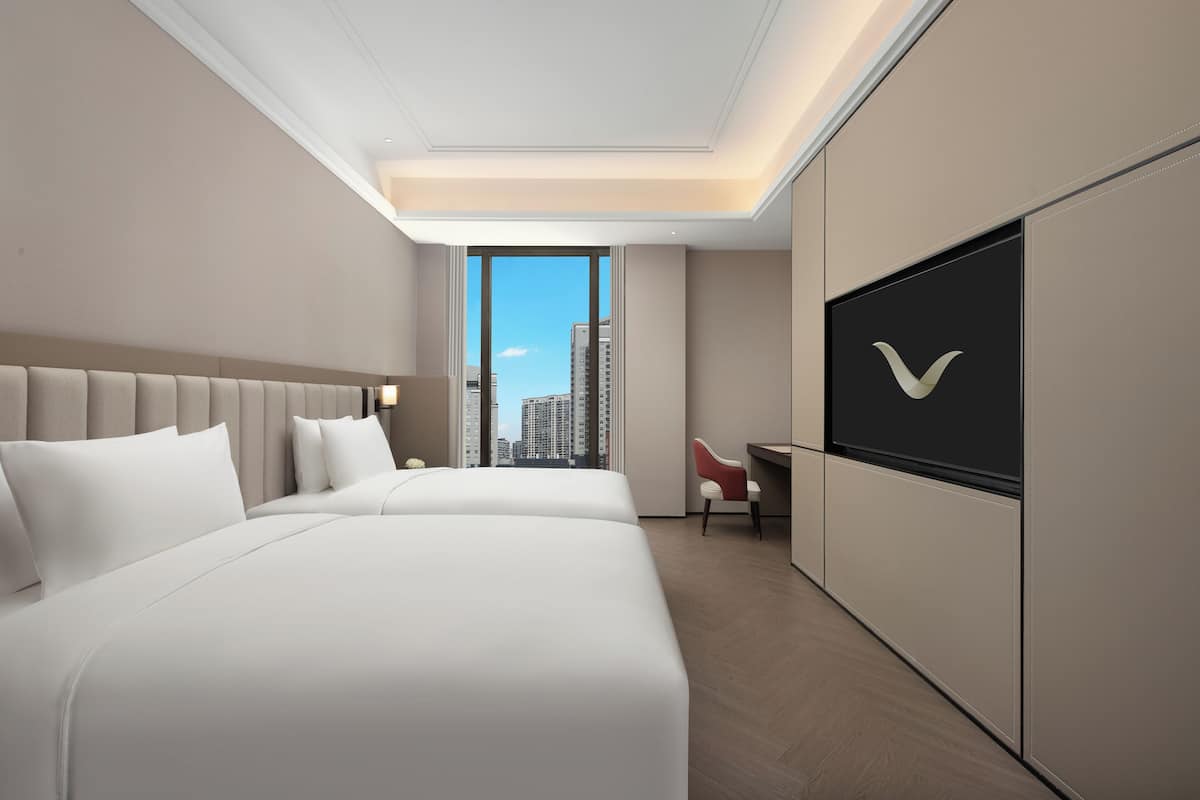 Une chambre d’hôtel avec deux lits, un bureau, une chaise et une grande fenêtre donnant sur la ville.
