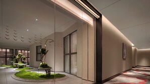 Un moderno vestíbulo de hotel con jardín central, paredes de vidrio y suelo estampado.
