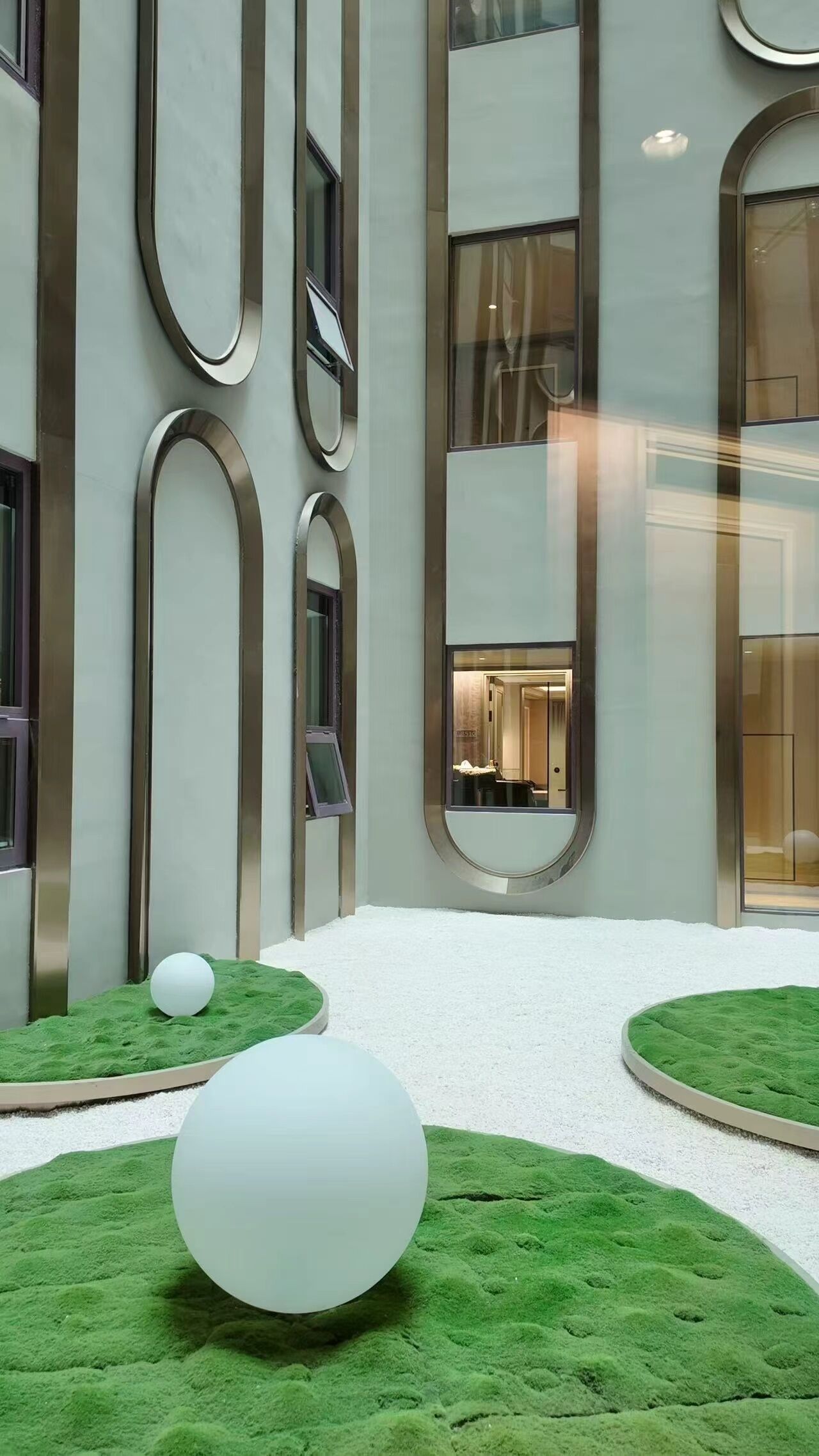 A modern building interior with a central courtyard featuring artificial grass and spherical objects.