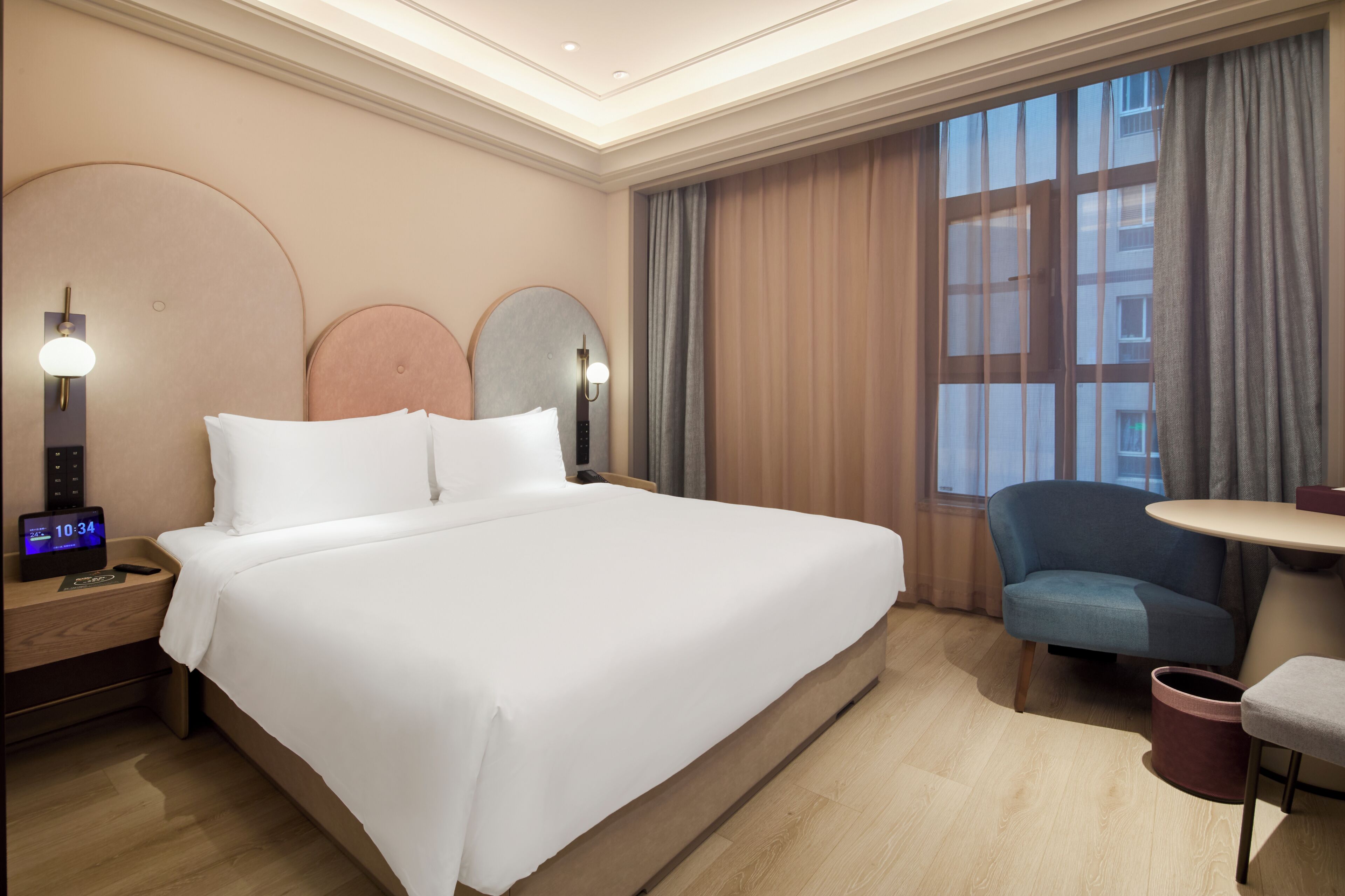 A hotel room with a large bed, bedside tables, a desk, a chair, a small table, and a window with curtains.