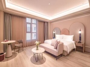 Une chambre d’hôtel avec un lit, une table de chevet, une lampe et une petite table sur laquelle est posé un vase de fleurs.