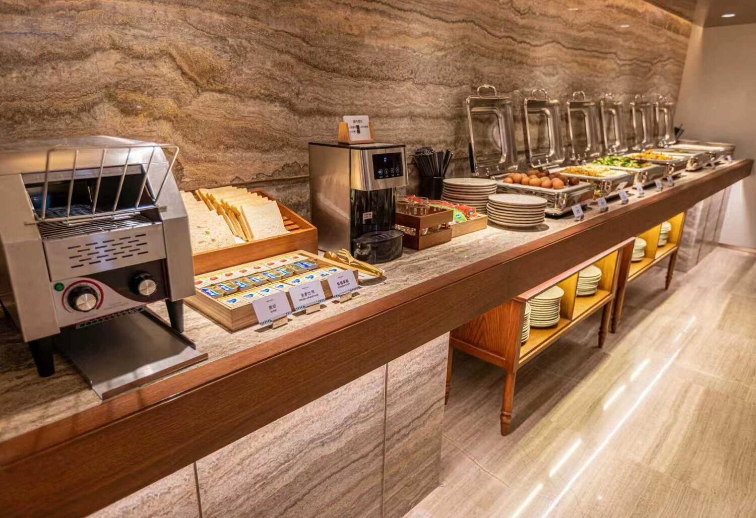 A buffet setup with a coffee machine, a variety of food items, and a marble wall background.