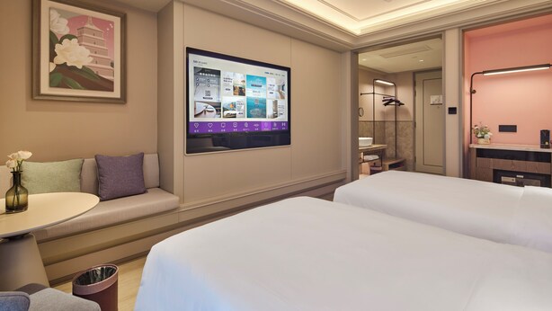 Quarto de hotel com um grande ecrã digital, um sofá, duas camas, uma pequena mesa e um cesto de lixo.
