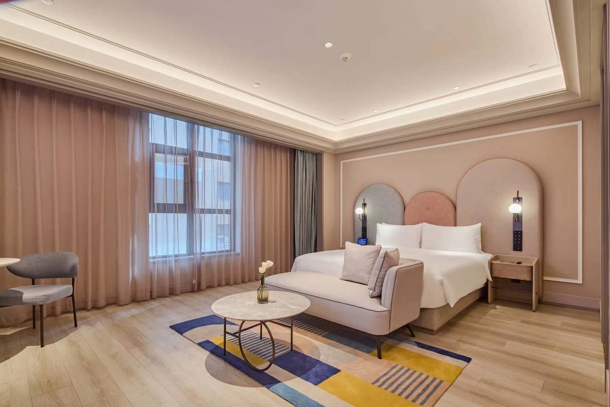 Hotelkamer met een bed, een bank, een kleine tafel, een stoel, een nachtkastje en een raam met gordijnen.