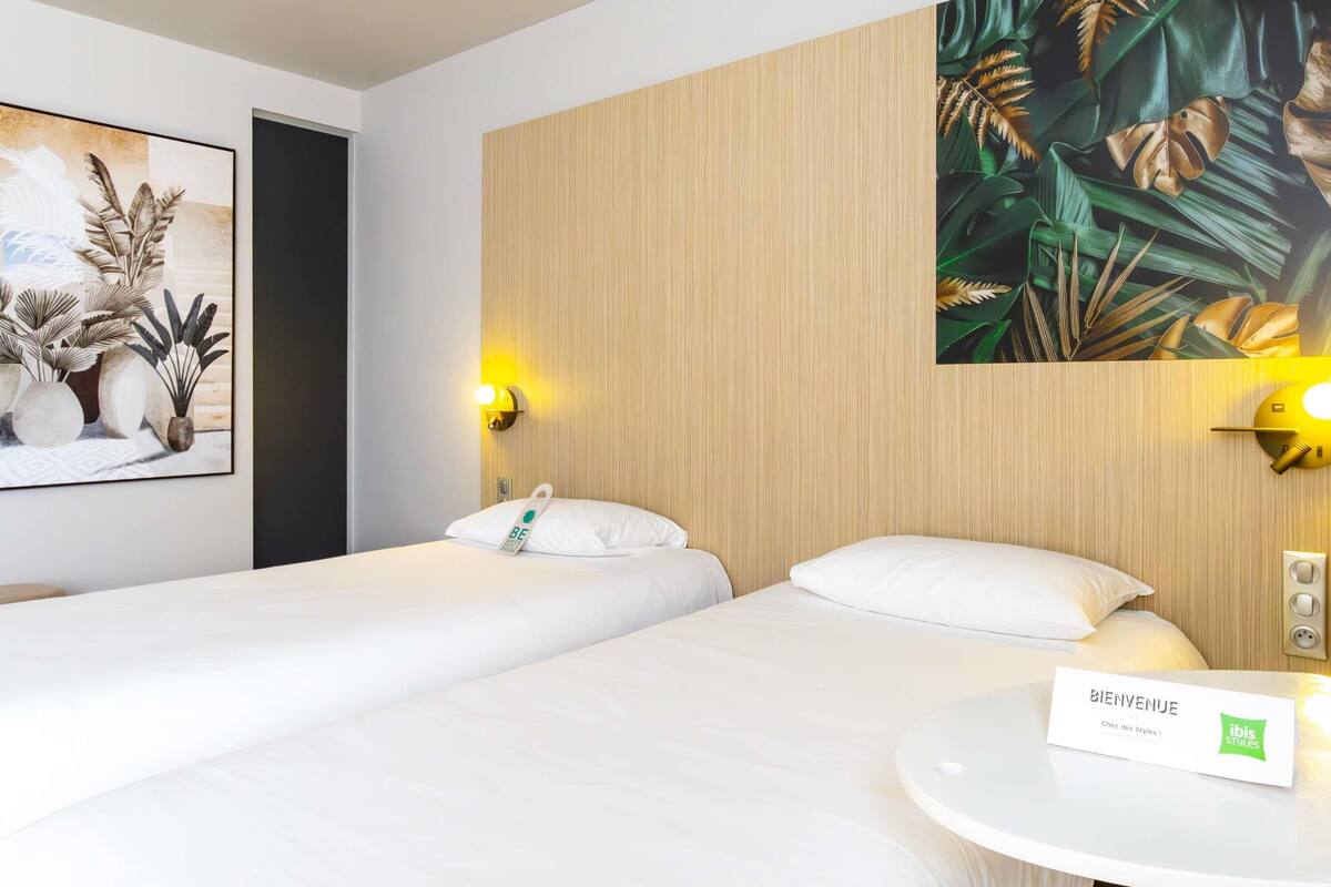 A hotel room with two beds, a round table with a sign, and a wall with a tropical plant mural.