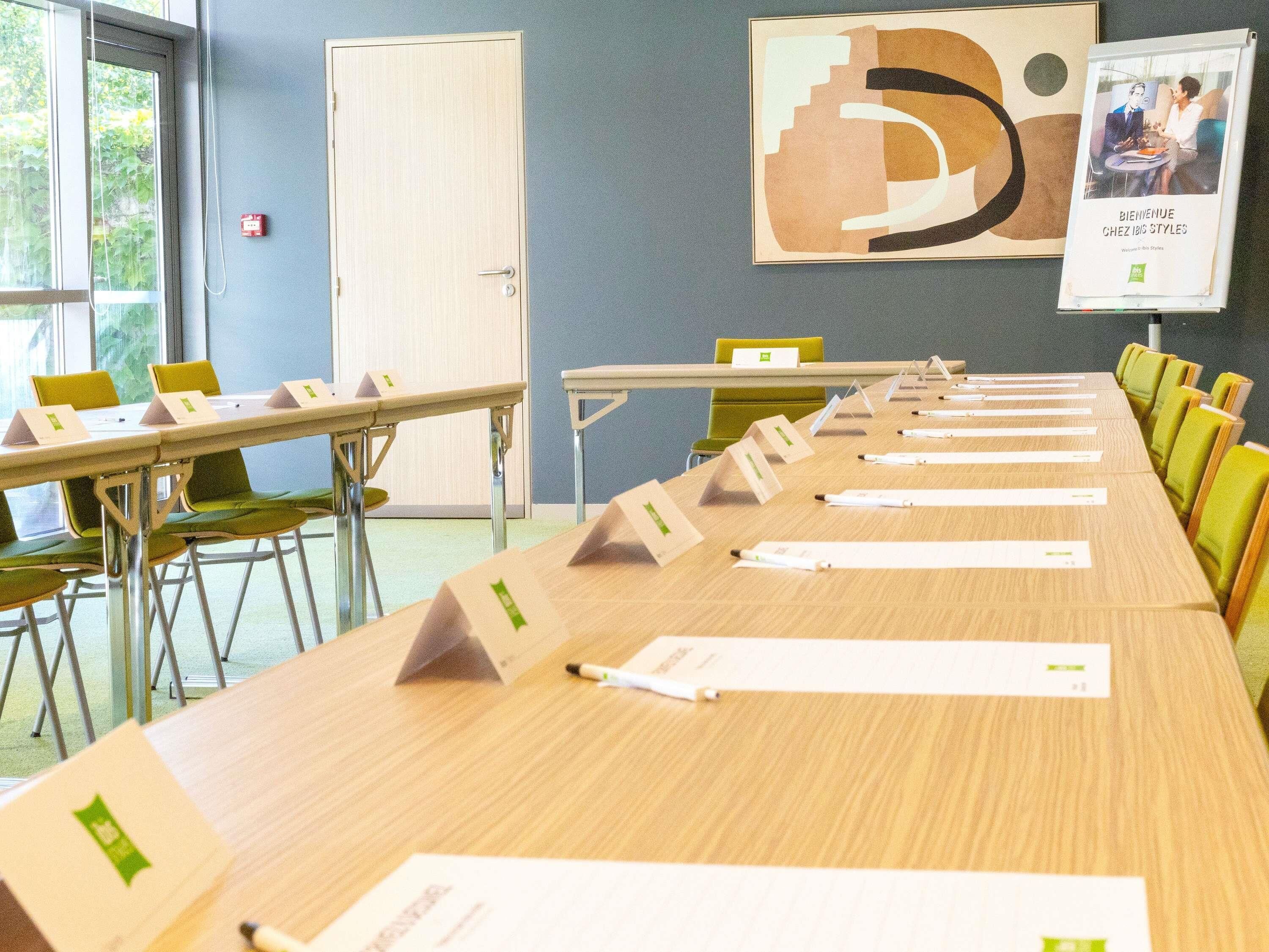 A conference room with a long table, chairs, nameplates, and a poster on the wall.