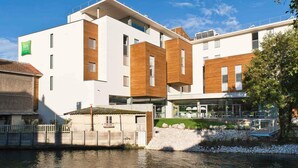 A modern building with a white facade and wooden accents, located near a body of water. - Ibis Styles Troyes Centre (Troyes)
