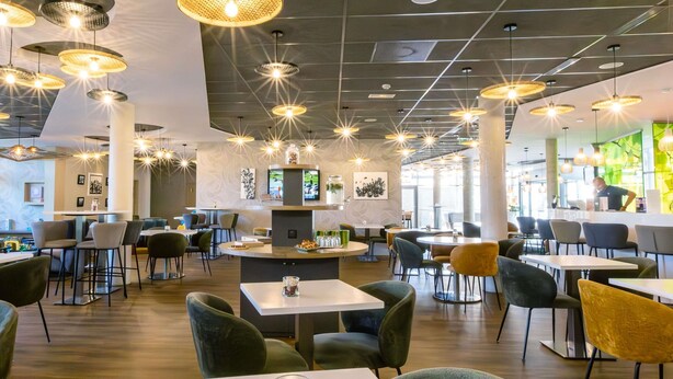 A modern restaurant with multiple seating areas, including round tables and chairs, and a central bar area. - Ibis Styles Troyes Centre (Troyes)