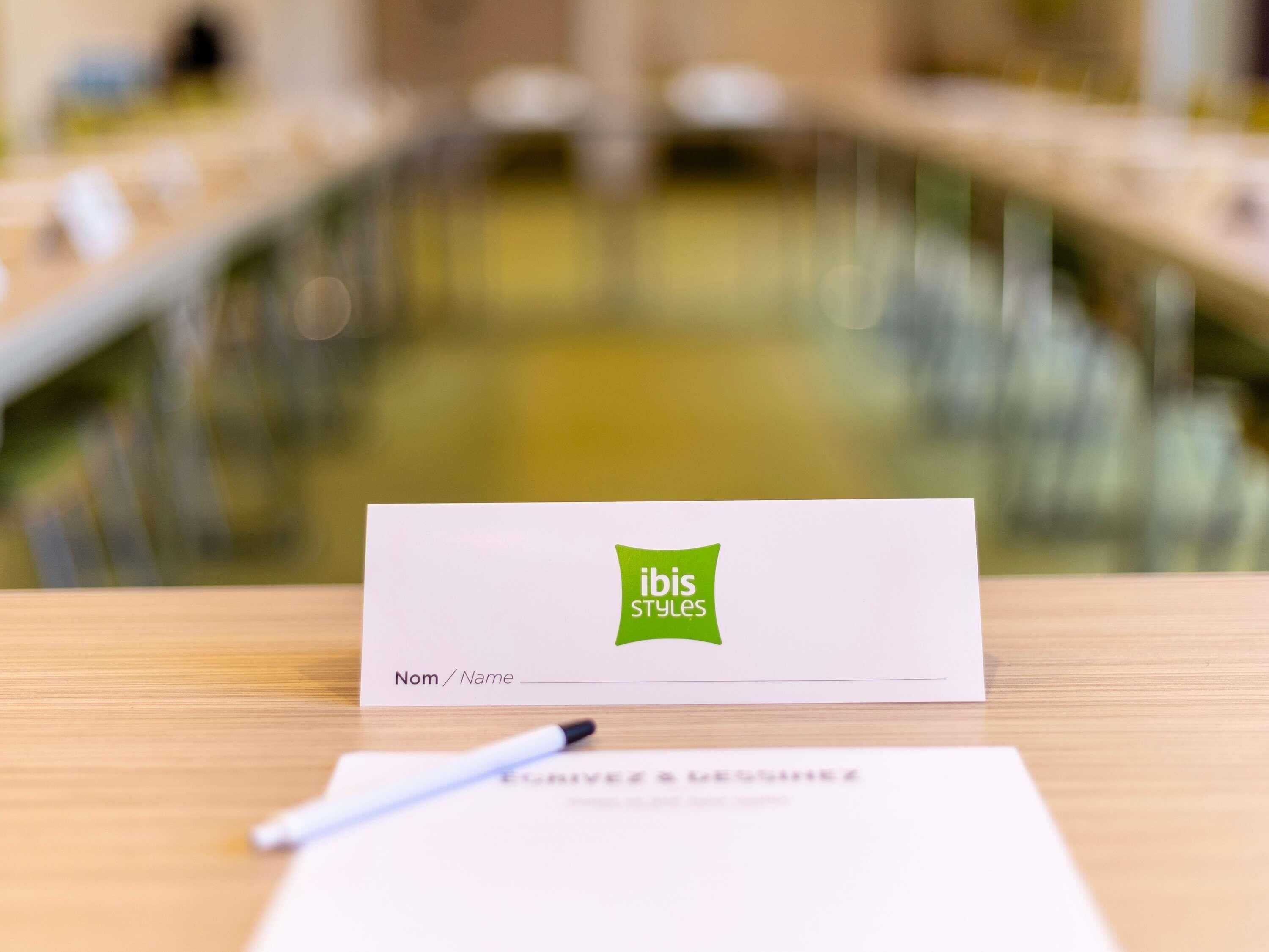 Tarjeta de presentación con el logotipo de 'ibis Styles' sobre una mesa de madera.