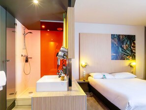 A hotel room with a shower, a sink, a bed, and a painting on the wall. - Ibis Styles Troyes Centre (Troyes)