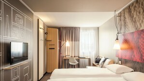 A hotel room with two beds, a desk with a chair, a TV, and a desk lamp. - Ibis Troyes Centre (Troyes)