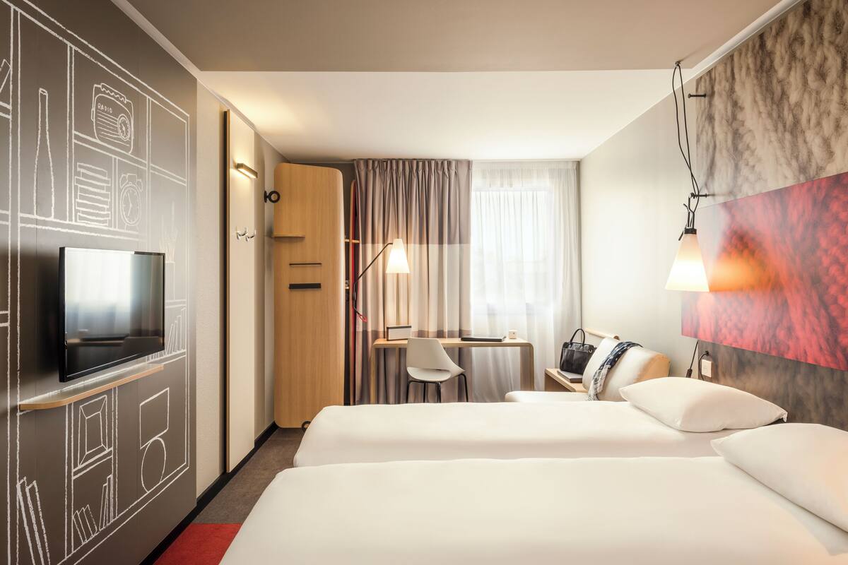 A hotel room with two beds, a desk with a chair, a TV, and a desk lamp.