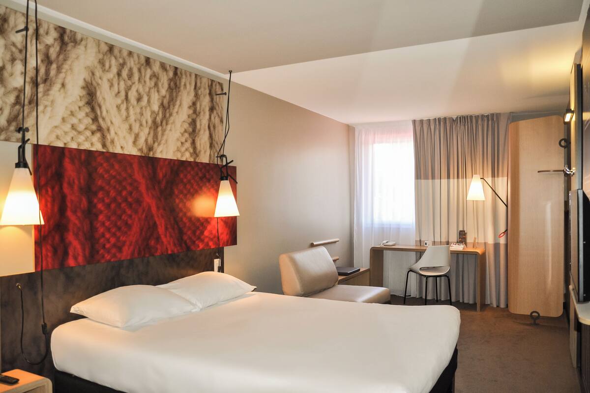 A hotel room with a large bed, a desk, a chair, and a TV.