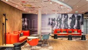 A modern lounge area with orange sofas, a round table, and a patterned rug. - Ibis Troyes Centre (Troyes)
