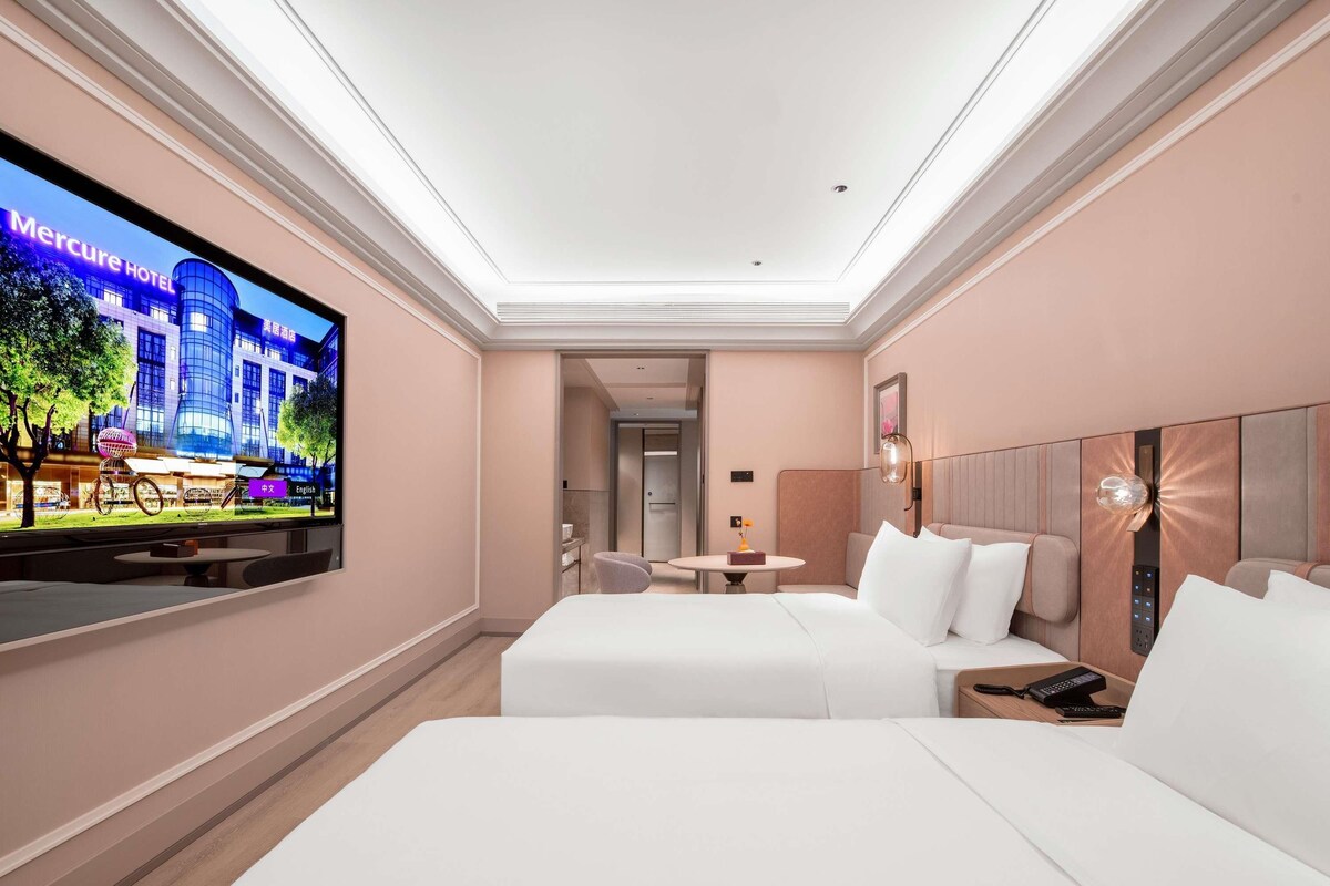Une chambre d’hôtel avec un grand téléviseur fixé au mur, un lit, une table de chevet et une petite table avec une chaise.