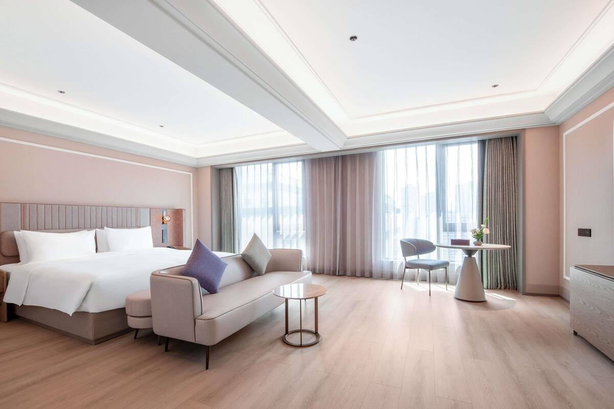 A modern hotel room with a large bed, a sofa, a small round table, and a chair.