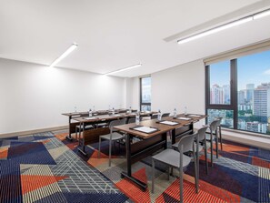 Une salle de conférence équipée de tables, de chaises et d’une grande fenêtre donnant sur la ville.