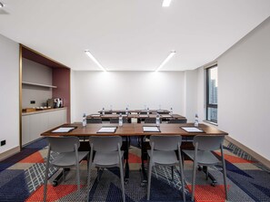 Une salle de conférence équipée d’une longue table, de chaises, de bouteilles d’eau et d’un coin café.
