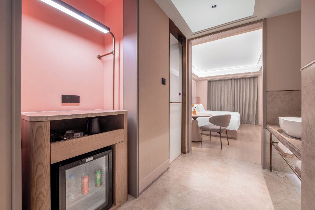 Una habitación de hotel moderna con minibar, zona de estar, ventana grande y baño con lavamanos amplio.