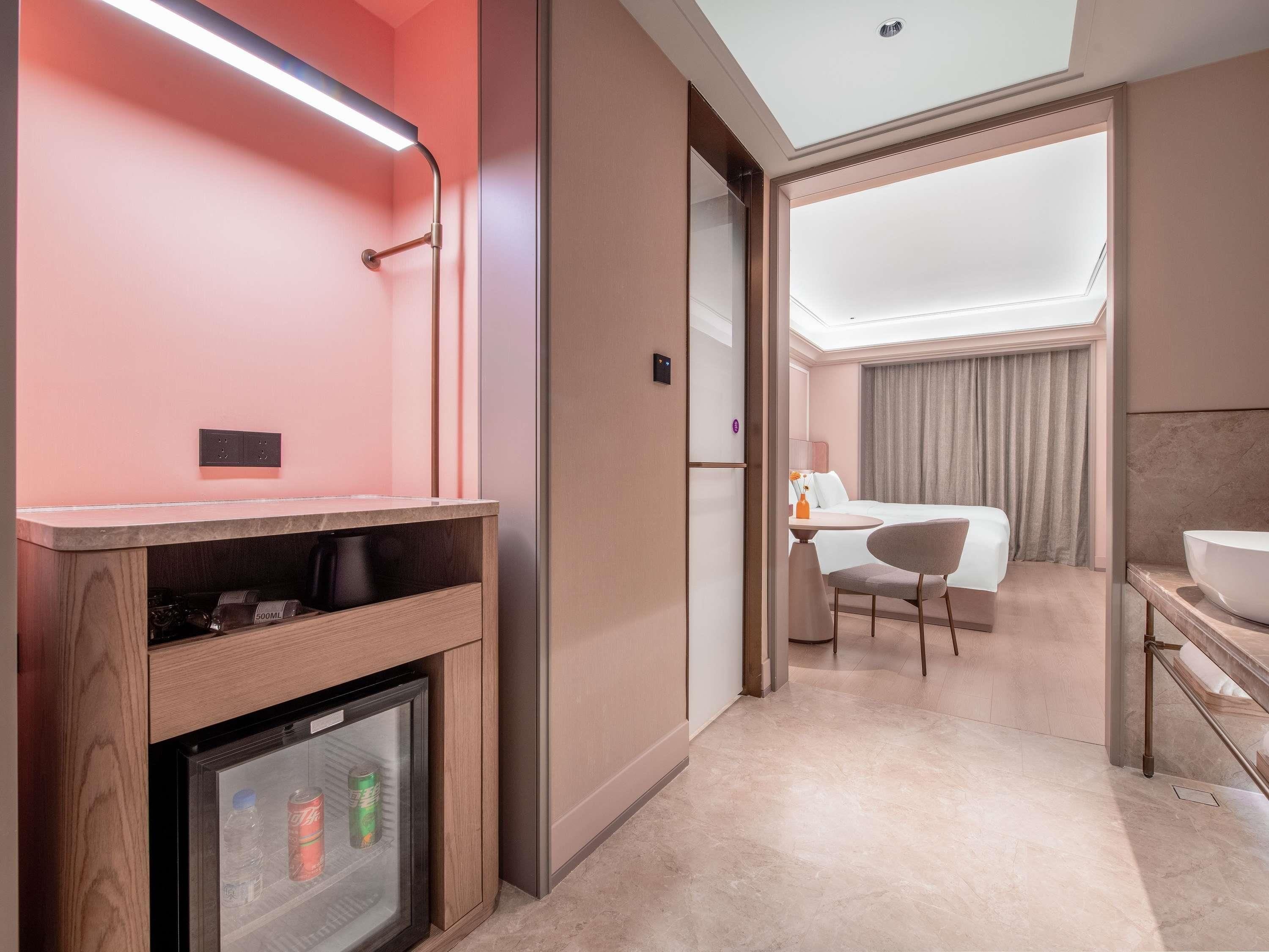Une chambre d’hôtel équipée d’un mini-bar, d’un réfrigérateur, d’un lit, d’une salle de bain et offrant une vue sur le hall d’entrée de l’hôtel.