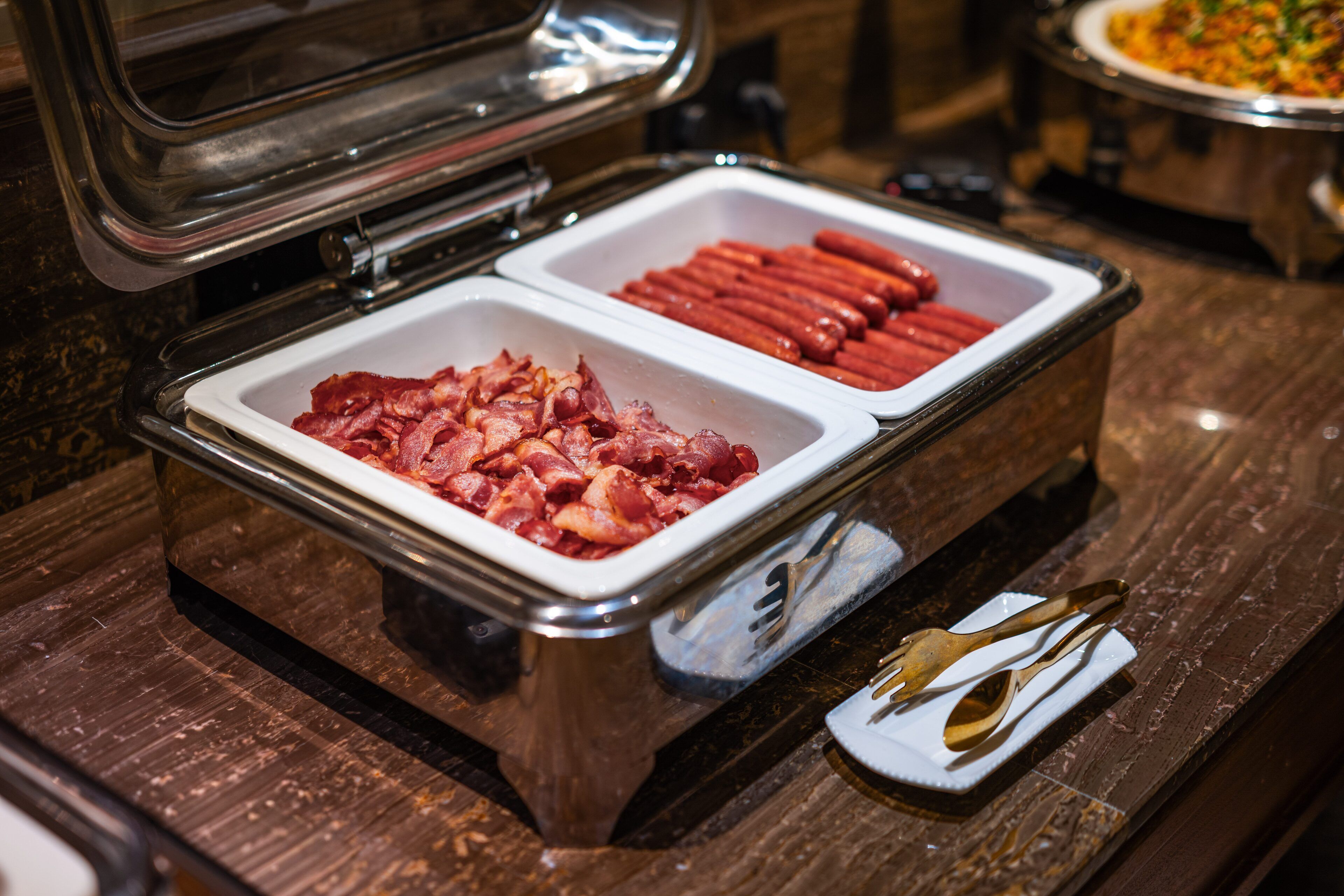 A buffet with two sections: one with bacon and the other with hot dogs.