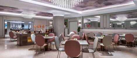A spacious dining area with modern chairs and tables, a central chandelier, and a view of the kitchen in the background.