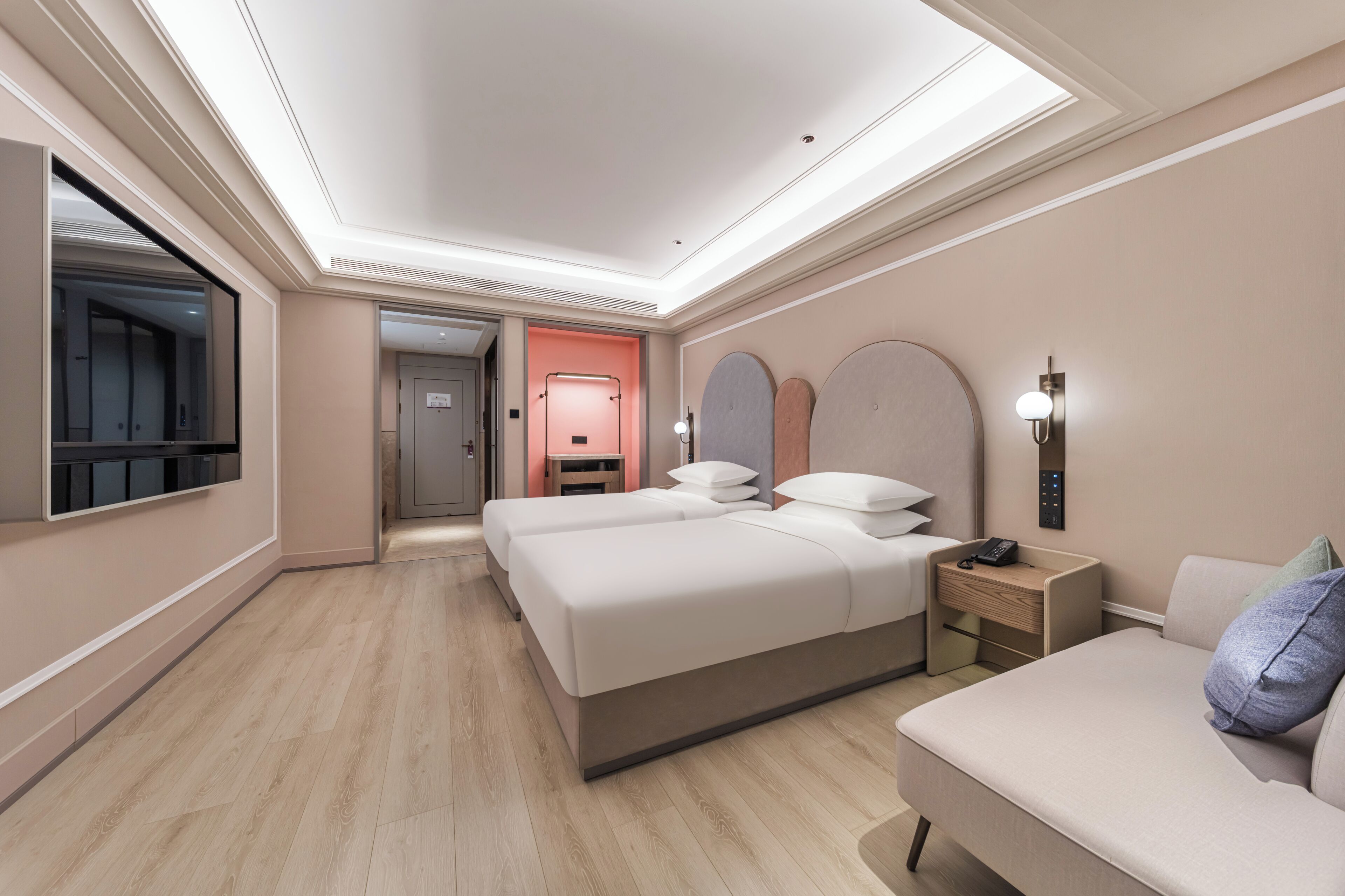 Habitación de hotel con dos camas, zona de estar, espejo, mesita de noche y teléfono instalado en la pared.