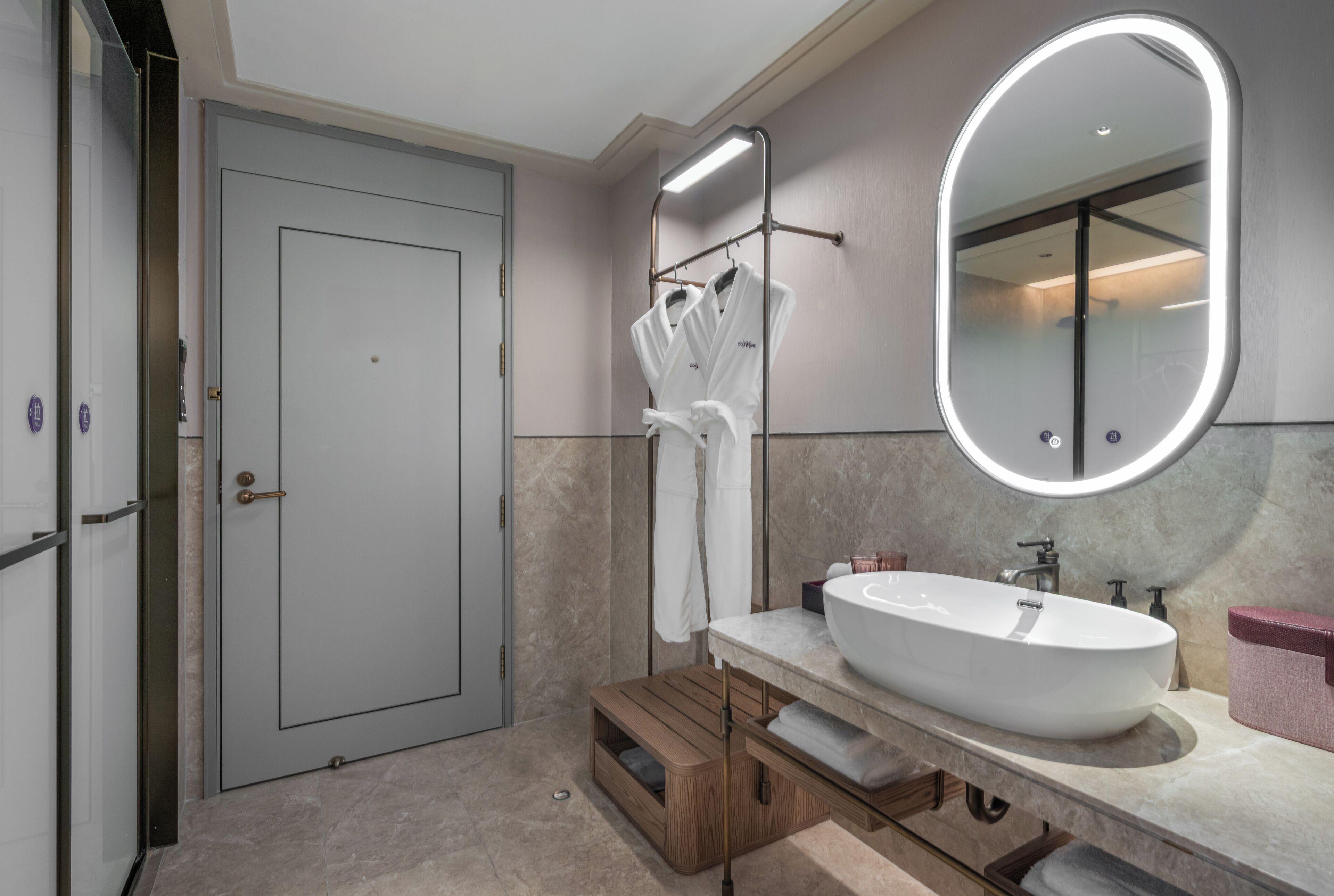 A modern bathroom with a large oval mirror, a white sink, and a wooden vanity.