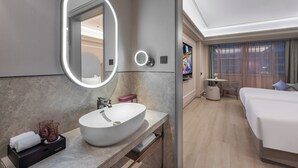 A modern hotel bathroom with a large oval sink, a mirror with integrated lighting, a vanity with a towel rack, and a small table with a vase. - Mercure Zhangjiajie Tianmen Mountain (Zhangjiajie)