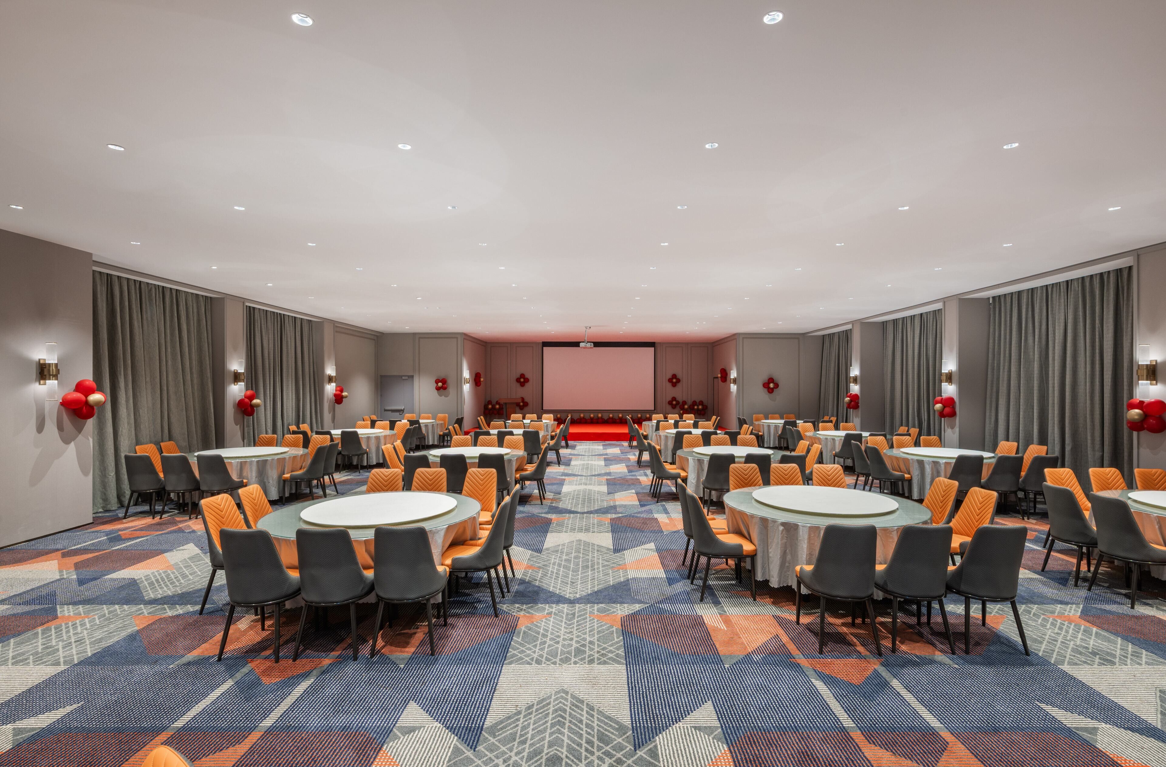 A conference room with round tables and chairs, a stage, and a patterned carpet.