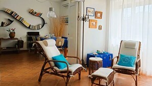 A living room with wicker furniture, a bookshelf, and a dining area with a table and chairs. - The Sea Outside (Alghero)