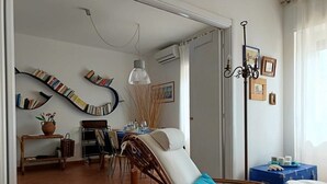 A living room with a dining area, wicker furniture, and a bookshelf. - The Sea Outside (Alghero)
