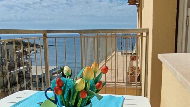 A balcony with a table set for two, a vase of tulips, and a view of the sea. - The Sea Outside (Alghero)