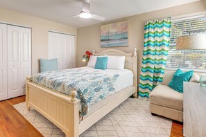 A bedroom with a bed, a ceiling fan, a window with curtains, and a wall-mounted artwork.