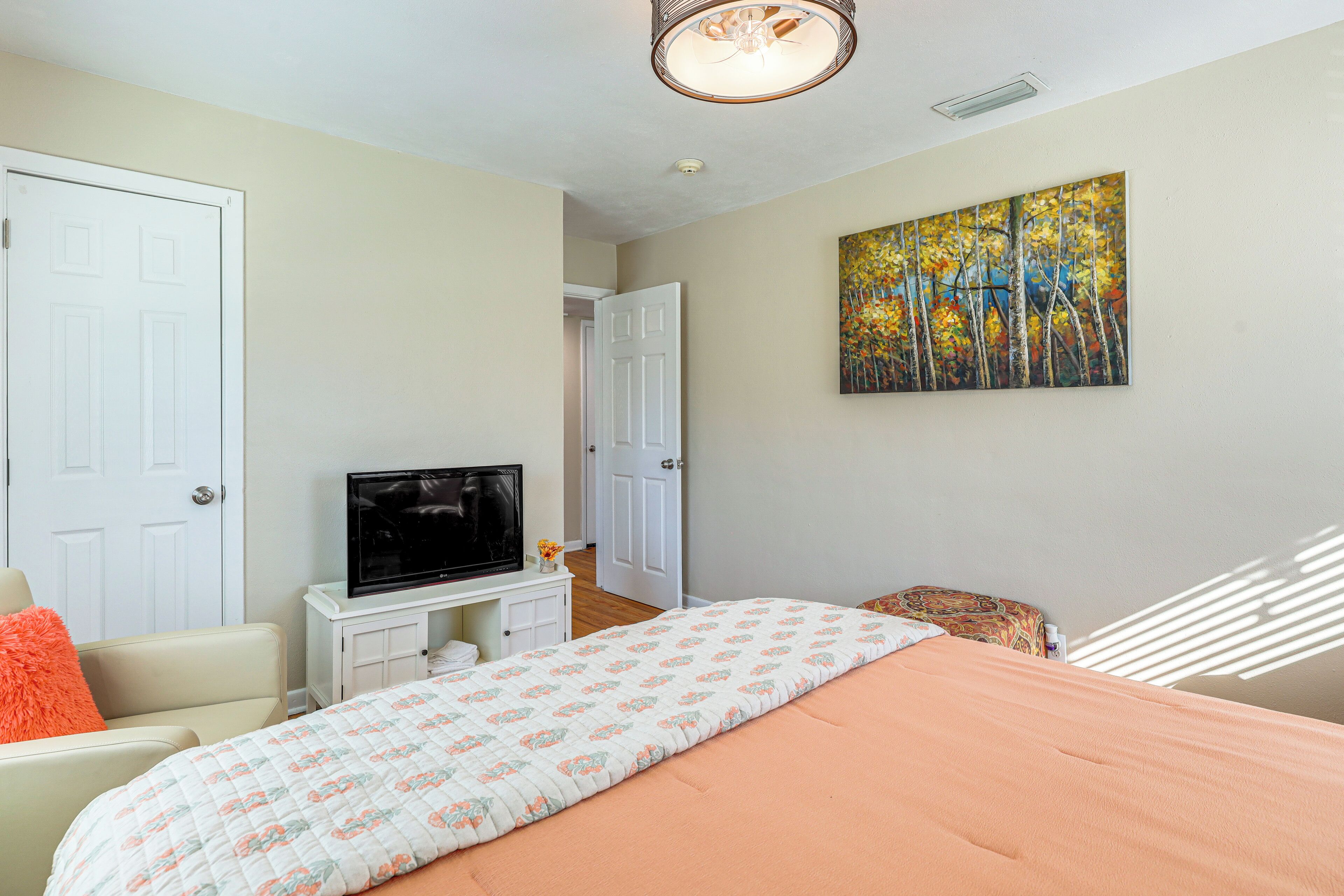 Une chambre à coucher avec un lit, un téléviseur posé sur un meuble, une porte et un tableau accroché au mur.