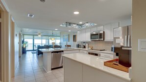 A modern kitchen with white cabinetry, a central island, and a dining area with a view. - 2BR Gulf-view Resort Condo: Suntide III - Unit 607 (South Padre Island)