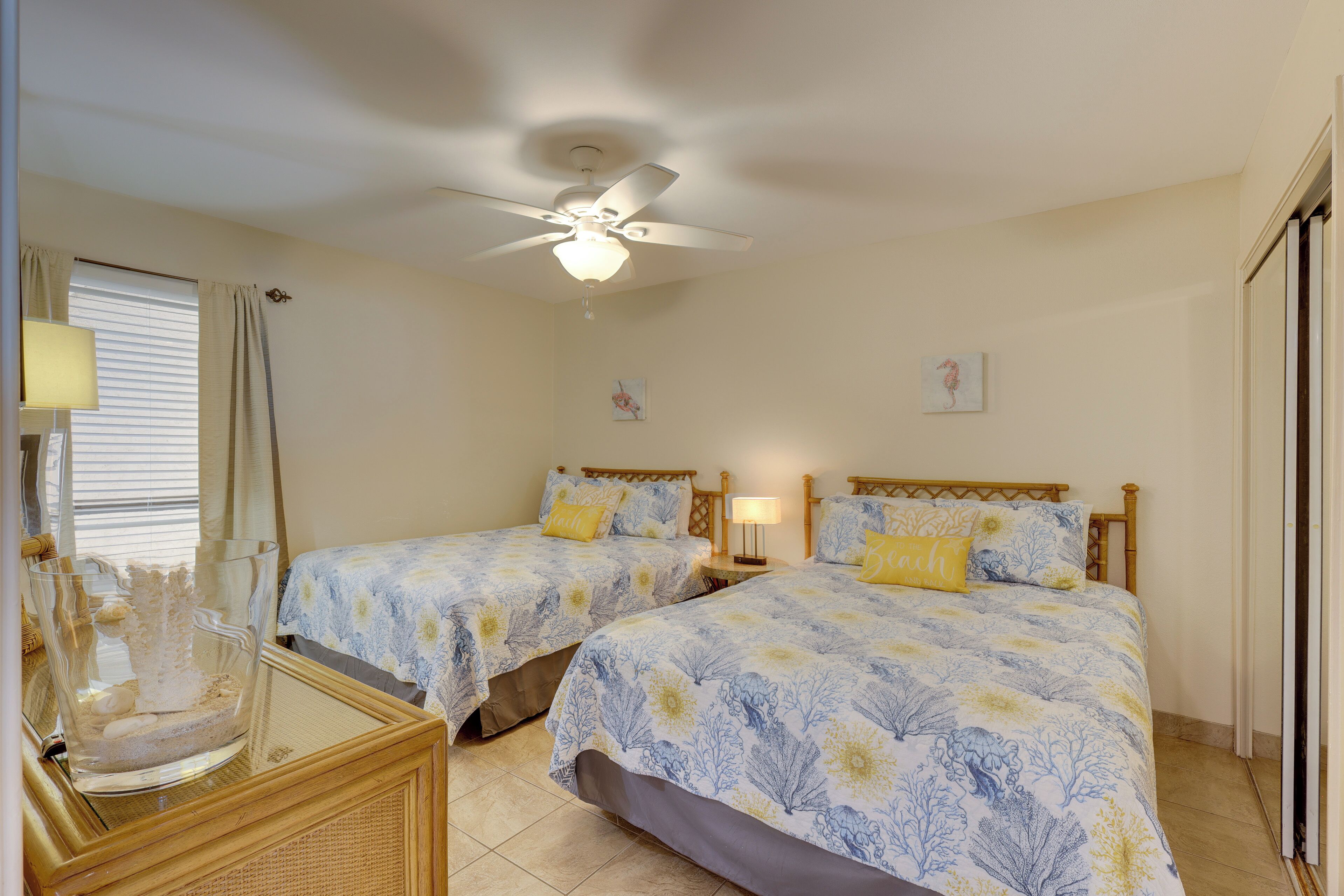 A bedroom with two beds, a ceiling fan, and a bedside table with a lamp.
