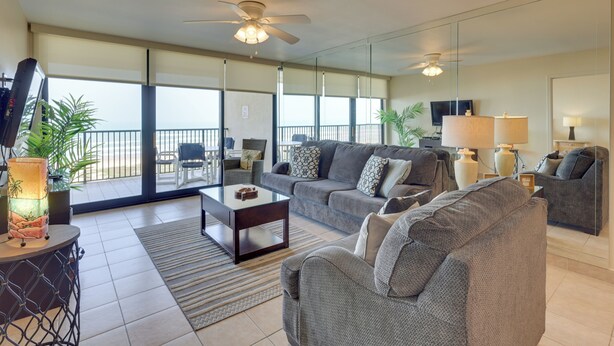 A spacious living room with a large sofa, a coffee table, and a TV. There is a balcony with a railing and potted plants. - 2BR Gulf-view Resort Condo: Suntide III - Unit 607 (South Padre Island)