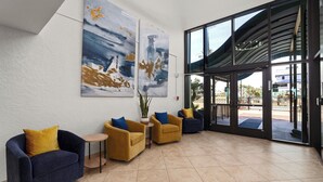 A lobby with a modern design, featuring a seating area with sofas and armchairs, a large window with a view of the outside, and two abstract paintings on the wall. - 2BR Gulf-view Resort Condo: Suntide III - Unit 607 (South Padre Island)