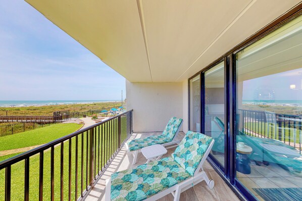 A balcony with two lounge chairs and a small table, overlooking a grassy area and the sea. - Gulf-view Condo w/ Perks: Suntide III - Unit 205 (South Padre Island)