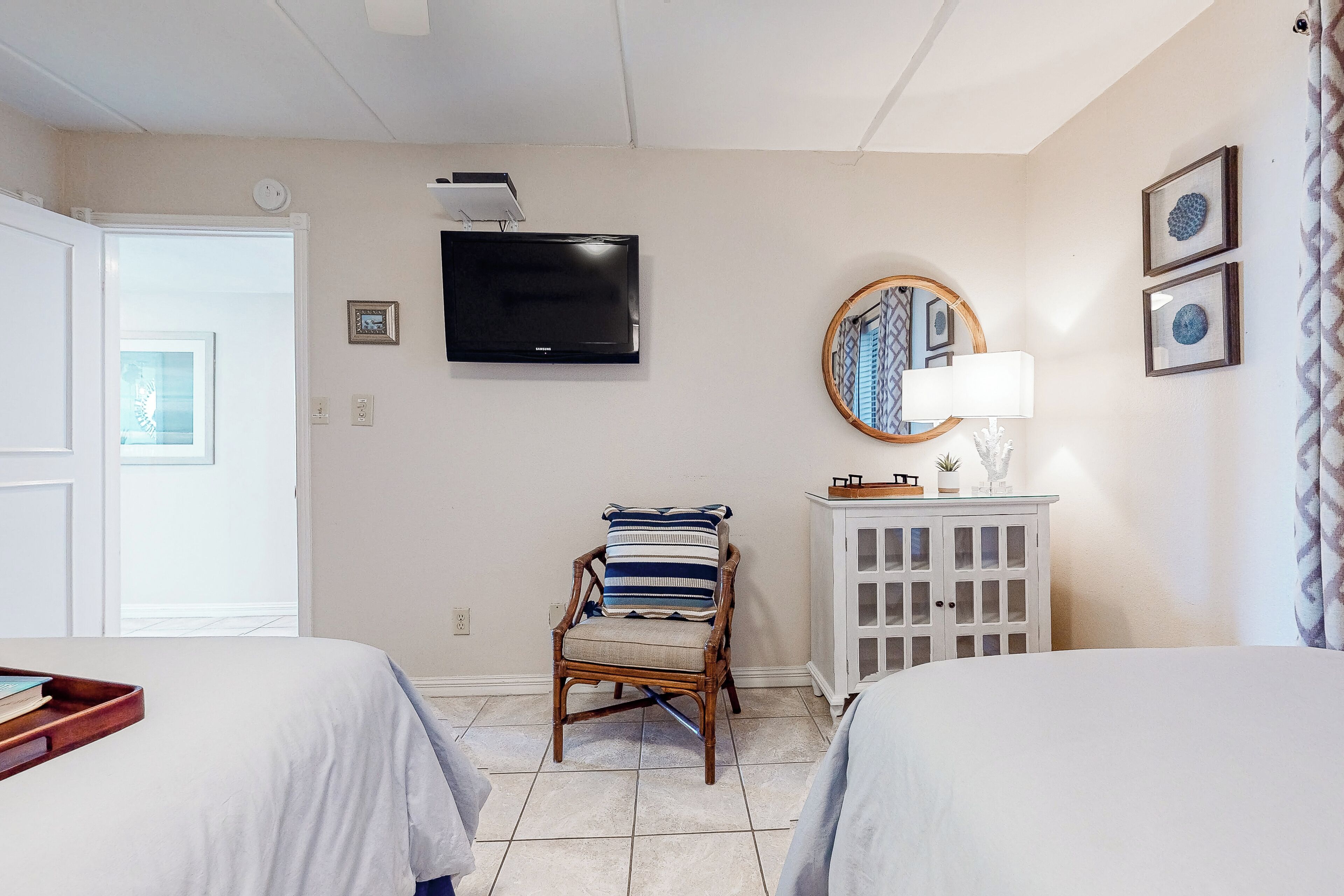 A bedroom with two beds, a television, a chair with a striped cushion, a cabinet, and a window with a view.